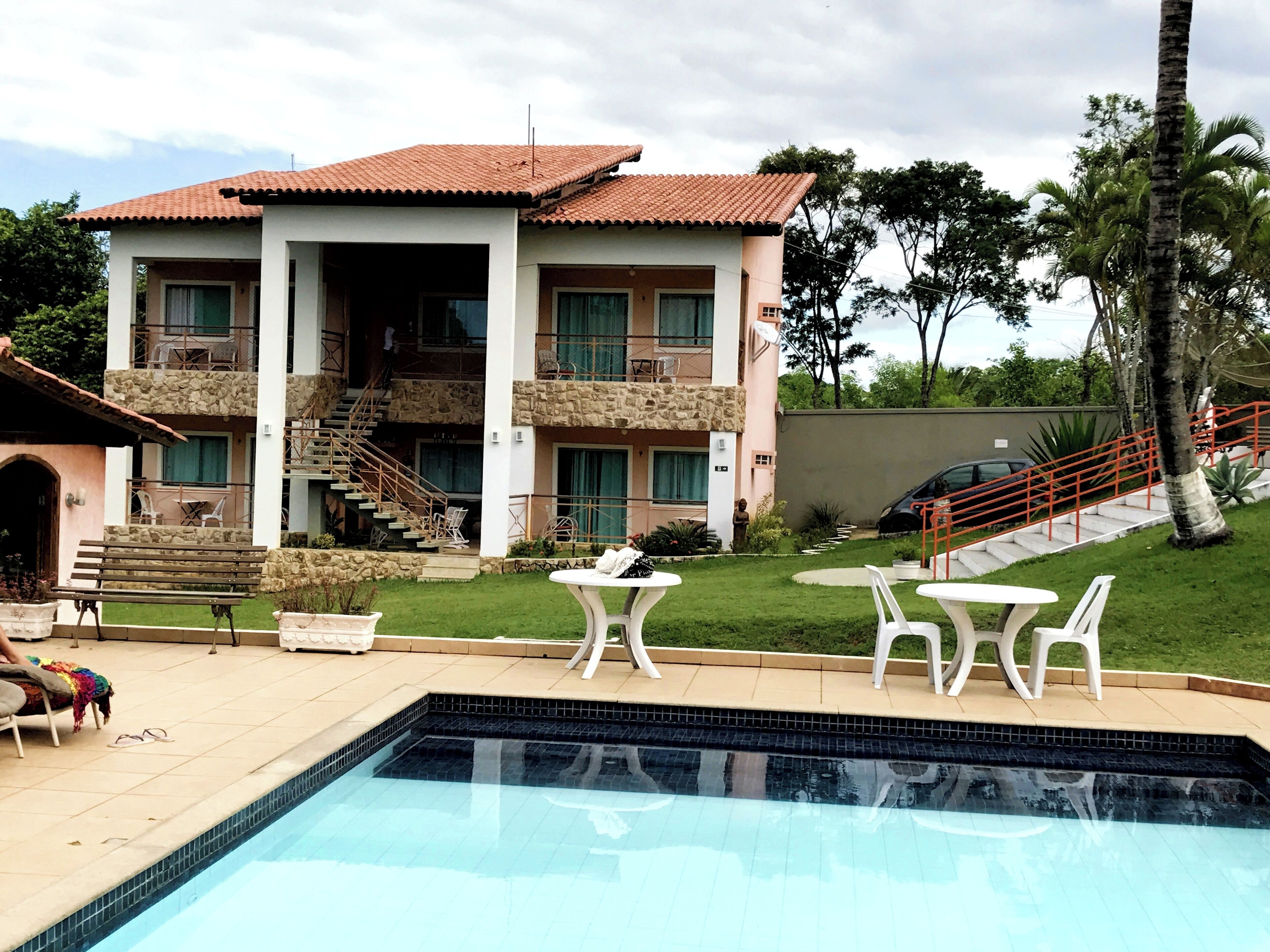 A hotel with a swimming pool, outdoor seating, and a staircase leading to the upper floors.