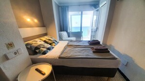 Ein Hotelzimmer mit Bett, einem kleinen Tisch und Meerblick durch ein Fenster.