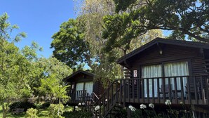 Two wooden cabins with balconies, surrounded by lush greenery and a clear blue sky. - Eight Bells Mountain Inn (Ruiterbos)