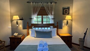 A hotel room with a wooden bed, two bedside tables, a telephone, a lamp, a window with curtains, and a framed picture on the wall. - Eight Bells Mountain Inn (Ruiterbos)