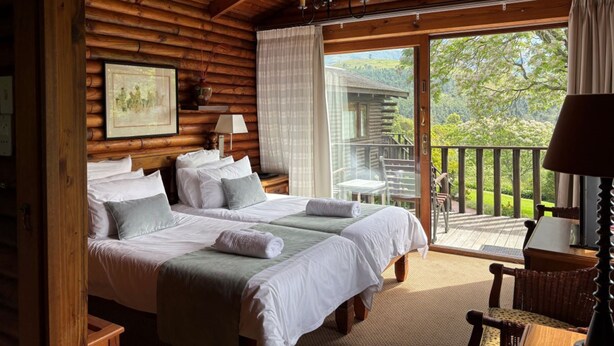 A log cabin bedroom with two beds, a large window, and a balcony. - Eight Bells Mountain Inn (Ruiterbos)