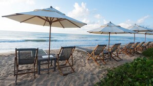 A beach with rows of lounge chairs and umbrellas, a wooden deck, and the ocean in the background. - Pousada Estrela D'Água (Porto Seguro)