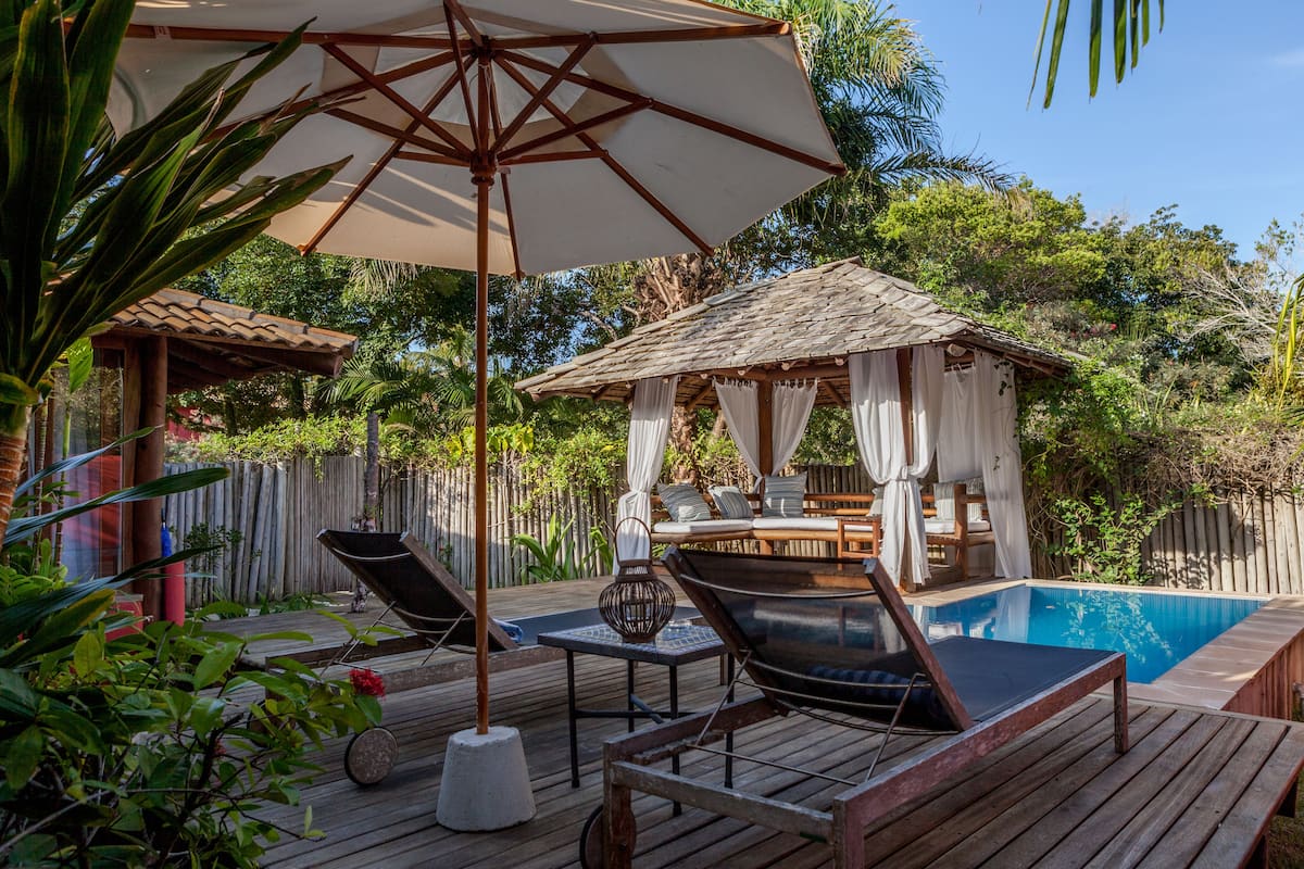 Eine Holzterrasse mit Liegestühlen, einem kleinen Pool und einem Pavillon mit Tisch und Stühlen.