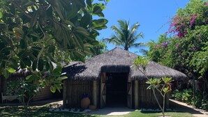 A thatched-roof structure with a wooden fence, surrounded by lush greenery and a clear blue sky. - Pousada Estrela D'Água (Porto Seguro)