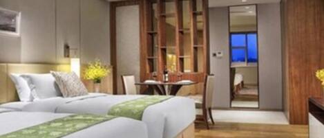 A modern hotel room with two beds, a dining area, and a view of the cityscape.