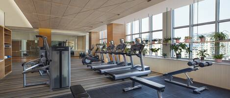 Une salle de sport moderne équipée de tapis de course, de vélos elliptiques et de poids libres.