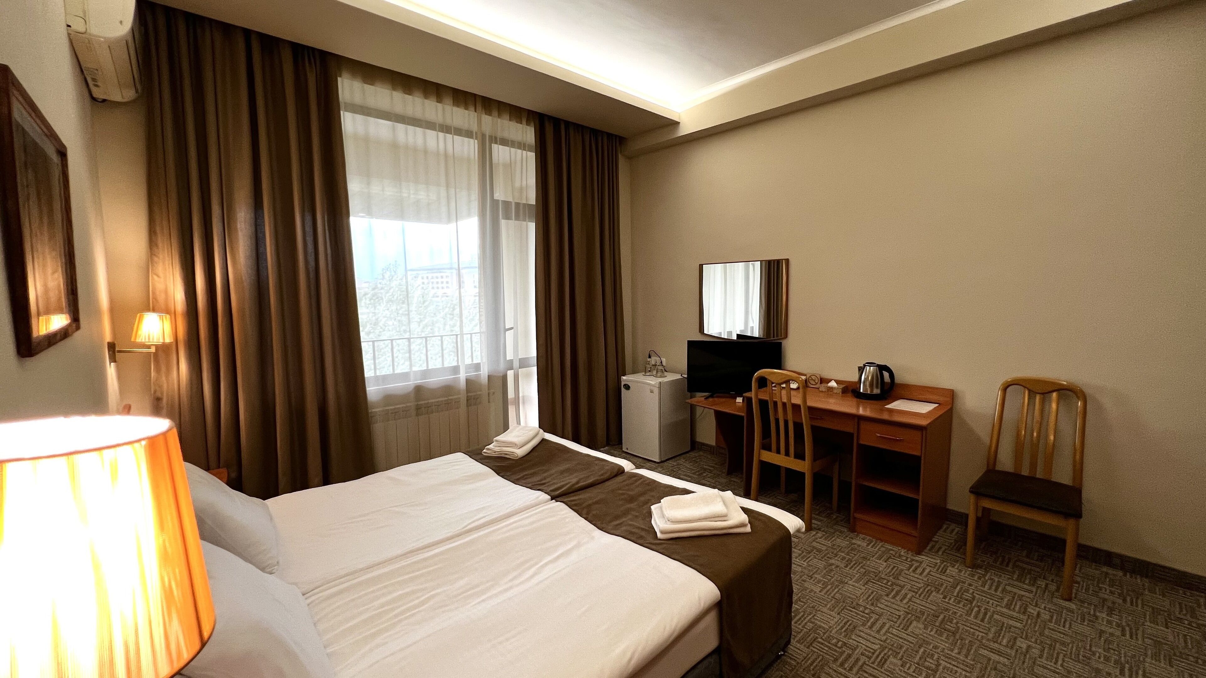 A hotel room with a bed, a desk, a chair, a television, and a window with curtains.