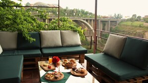 A balcony with green cushioned seating, a table with food and drinks, and a view of a bridge and greenery. - Olympia Hotel (Yerevan)