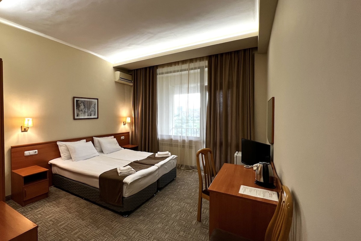 A hotel room with a large bed, a desk with a chair, a television, and a picture on the wall.