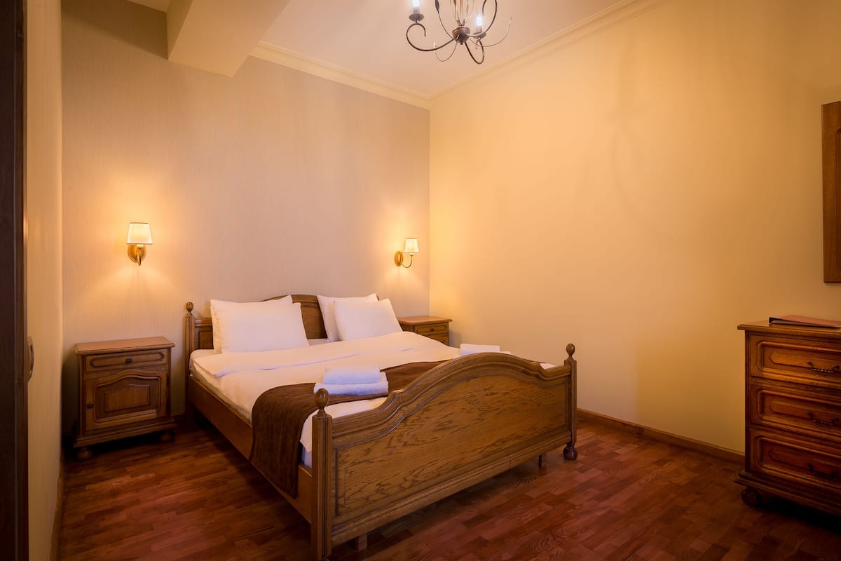 A bedroom with a wooden bed, two bedside tables, a nightstand, and a dresser.