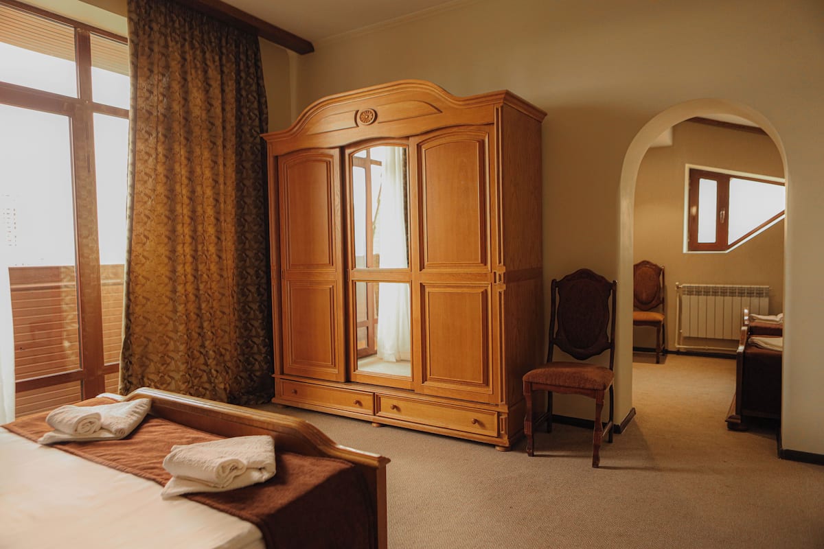 A hotel room with a bed, a wooden wardrobe, a chair, and an arched doorway.