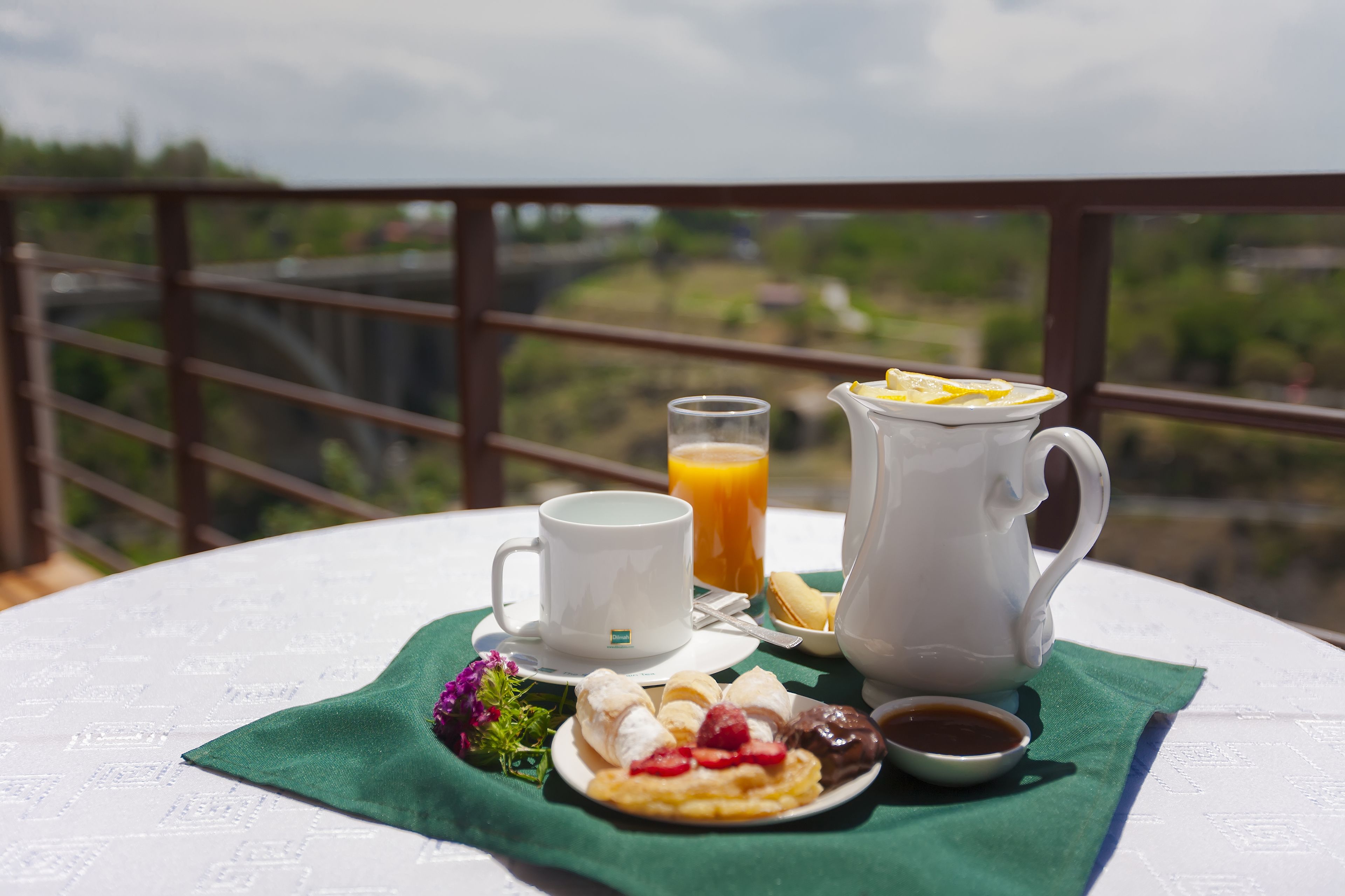 A breakfast setup on a balcony with a scenic view, including a cup, jug, and plate with food and drink.
