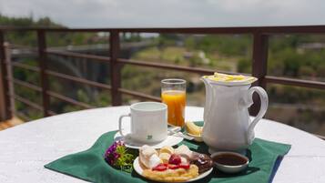 A breakfast setup on a balcony with a scenic view, including a cup, jug, and plate with food and drink.