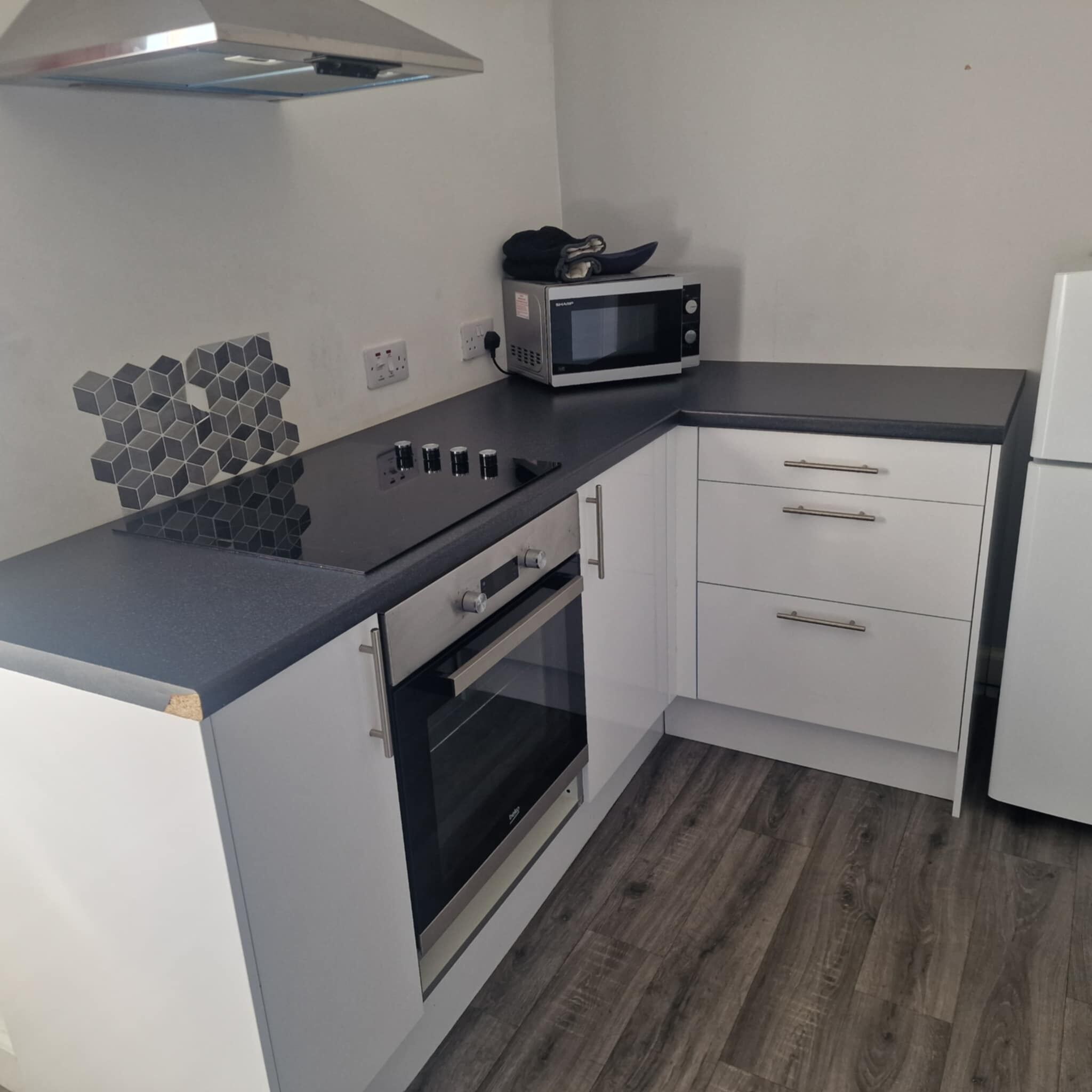 A compact kitchen with a microwave, oven, and a unique hexagonal tile backsplash.
