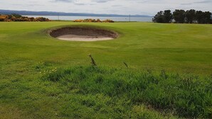 A golf course with a sand bunker and a view of the water and hills in the background. - Black Isle Holiday Apartments (Avoch)
