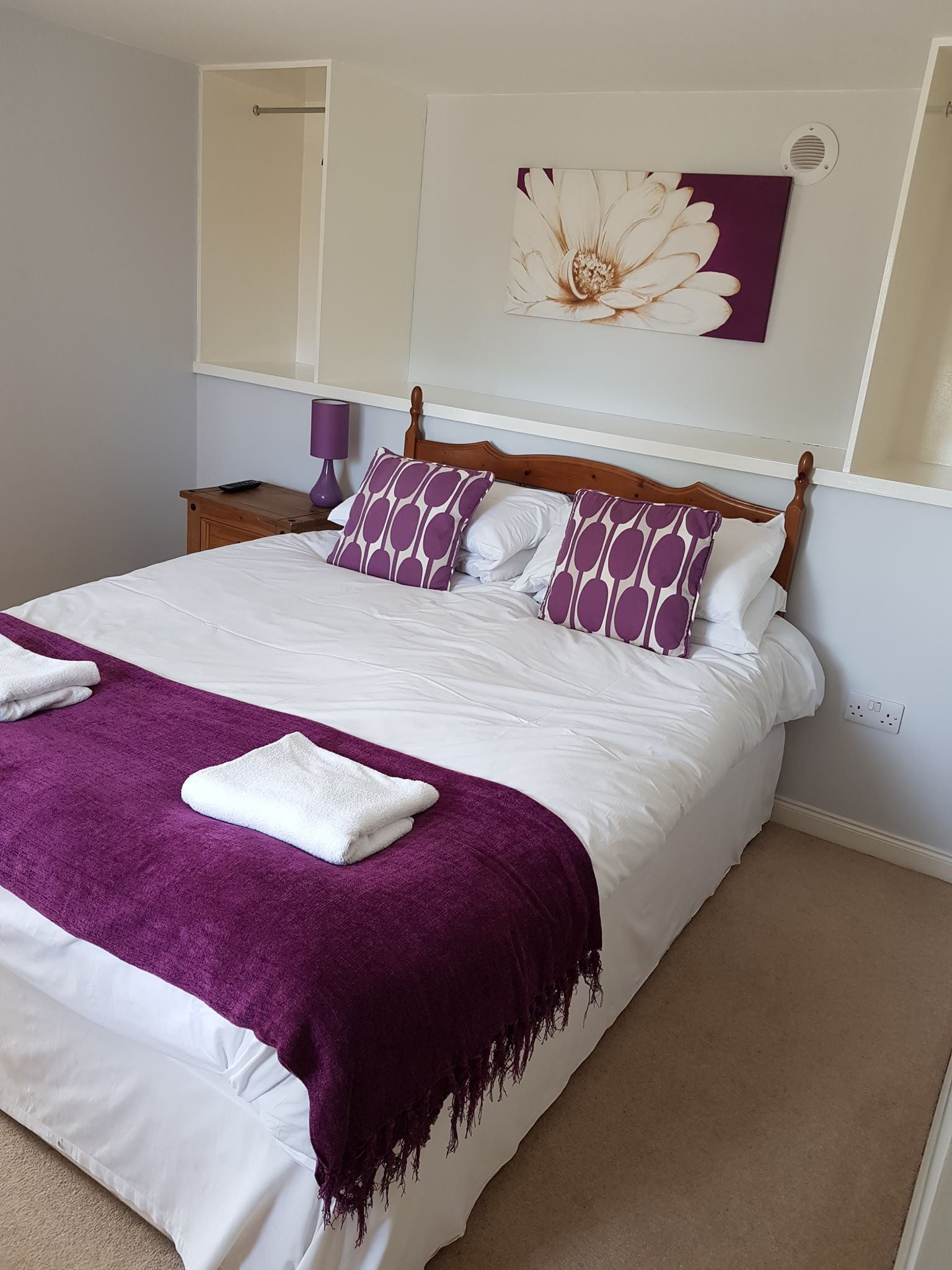 A neatly made bed with white and purple bedding, a purple throw blanket, and two white towels.