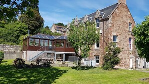A large stone building with a glass conservatory and a wooden deck. - Black Isle Holiday Apartments (Avoch)