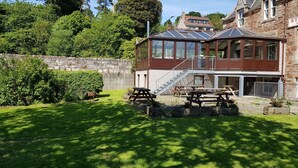 A two-story stone building with a covered patio area featuring picnic tables and a staircase leading to a balcony. - Black Isle Holiday Apartments (Avoch)