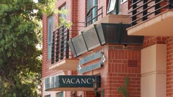 Un edificio de ladrillo rojo con un cartel de 'VACANCY', una entrada con rejas y un pequeño árbol en frente.