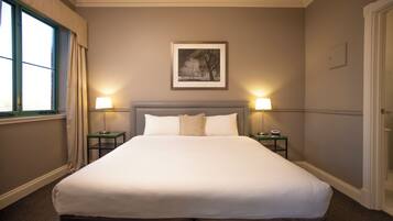 Habitación de hotel con una cama grande, dos mesitas de noche, un cuadro en la pared y una ventana con cortinas.