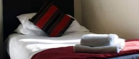 A neatly made bed with white linens, a red and black striped pillow, and a folded white towel.