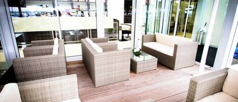 A modern indoor lounge area with wicker furniture, glass doors, and a view of the outside.