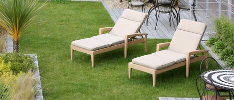 A patio area with two wicker lounge chairs and a round table with chairs.