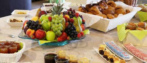 A buffet table with various food items including fruits, pastries, and condiments.