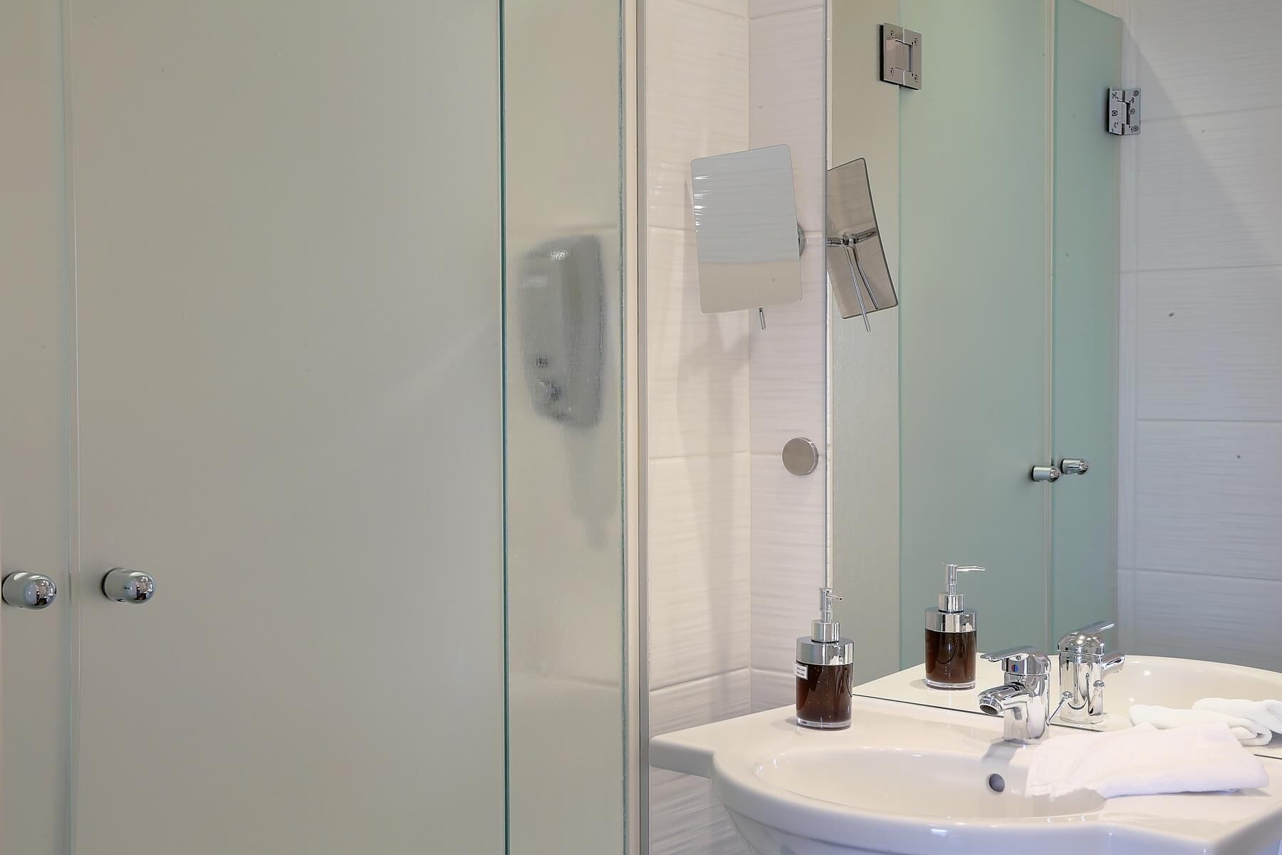 A modern bathroom with a glass shower enclosure, a white sink with a mirror, and a towel rack.