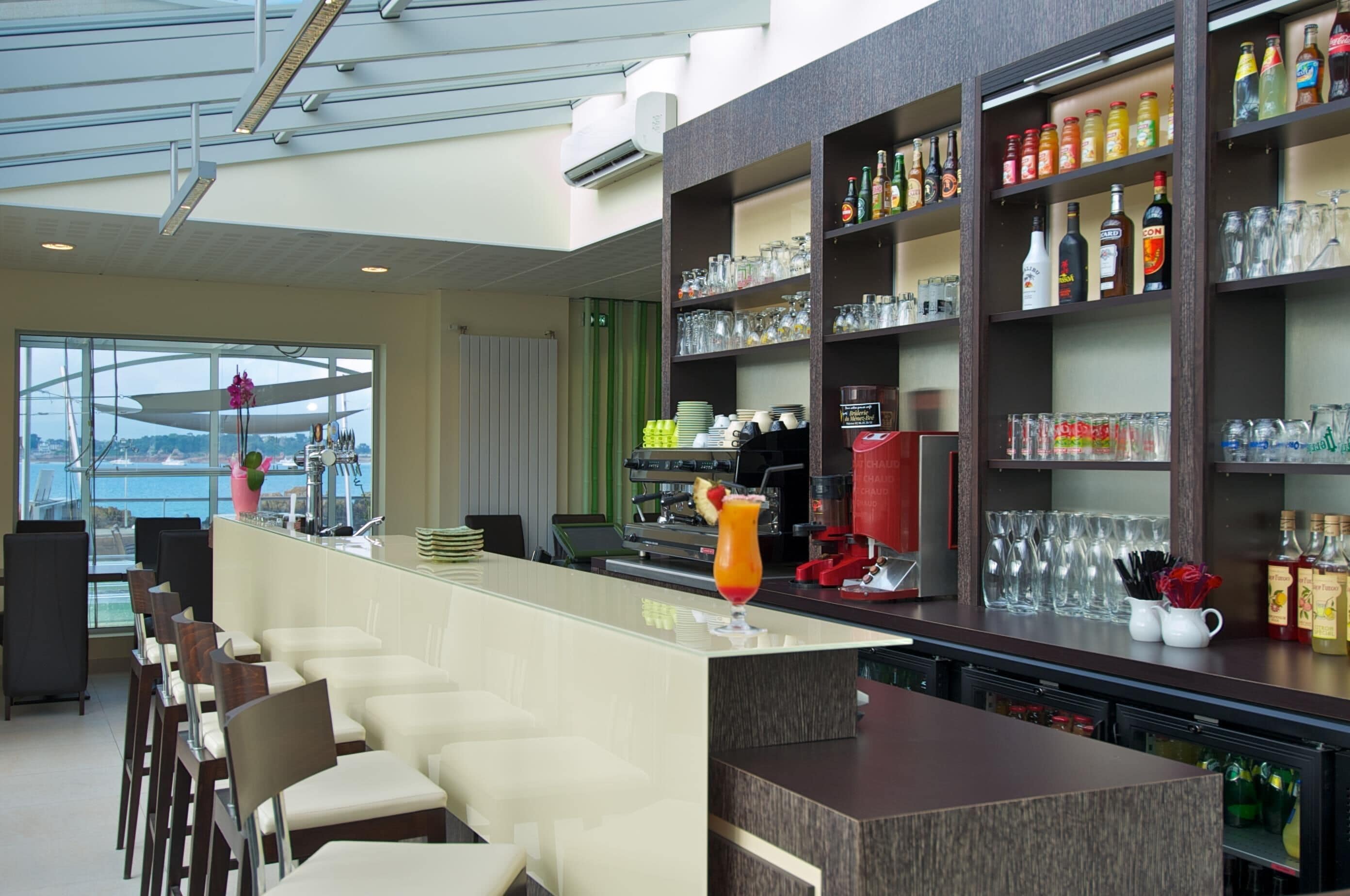 A bar area with a long counter, bar stools, and shelves stocked with bottles and glasses.