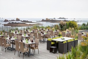 Un área de comedor al aire libre con mobiliario de mimbre y vistas al mar.