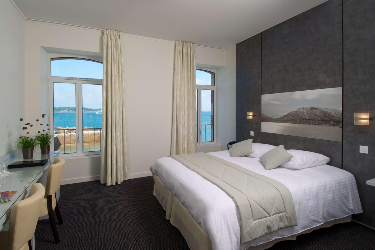 Una habitación de hotel con una cama grande, un escritorio con una silla y vista al mar.