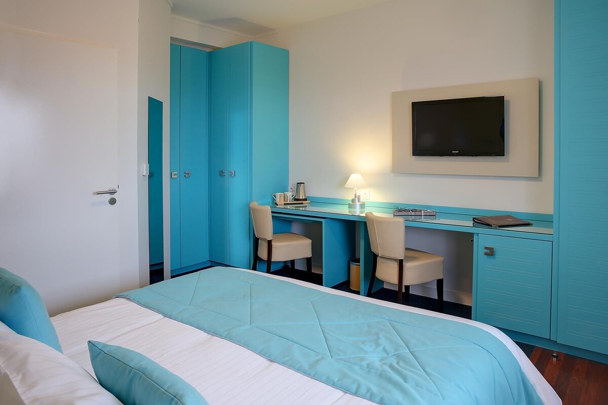 Una habitación de hotel con cama, un escritorio con dos sillas, televisión y armario.