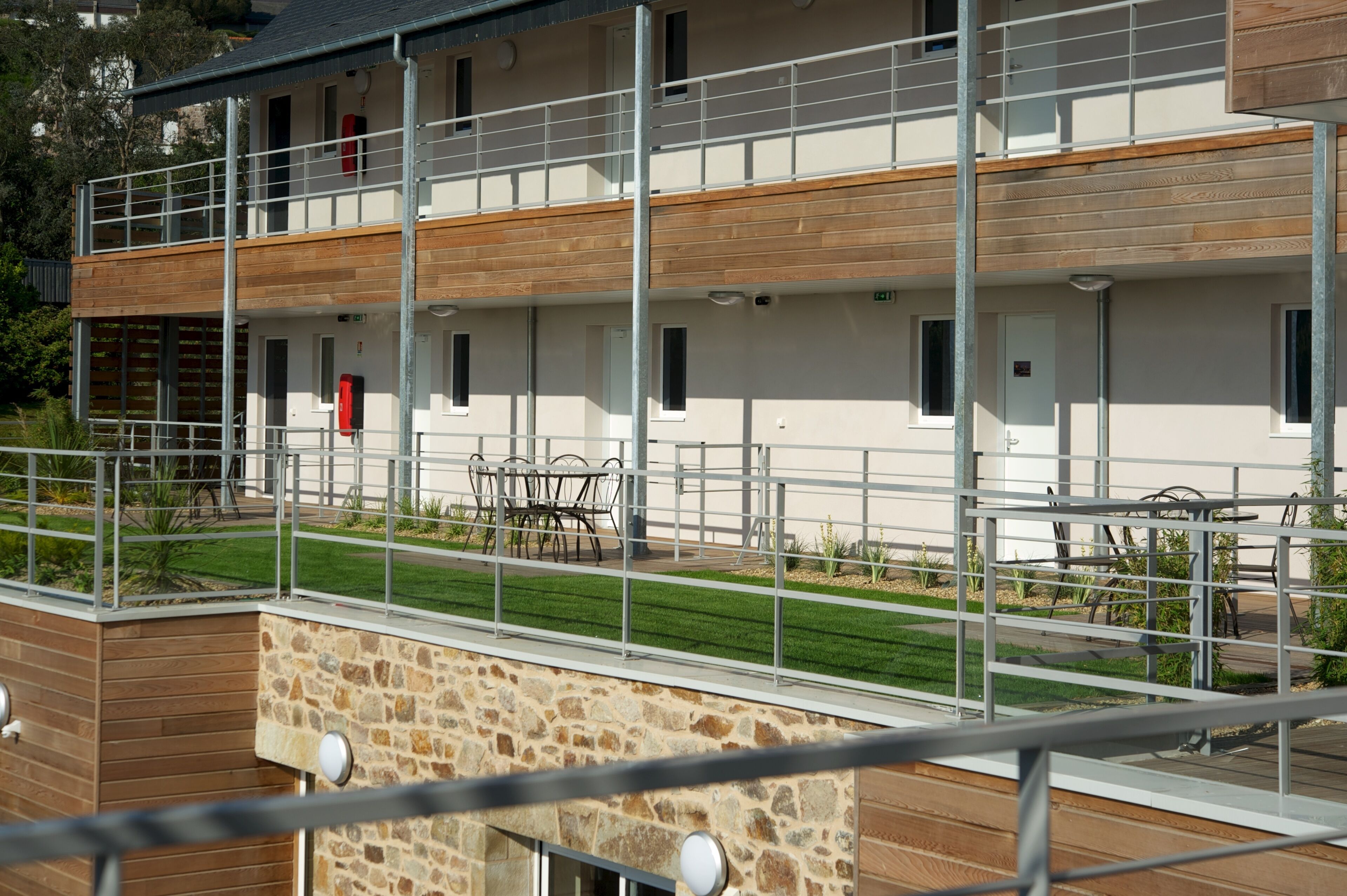 Un bâtiment moderne à la structure à deux étages, doté d’un espace extérieur aménagé pour s’asseoir et d’une façade en pierre.