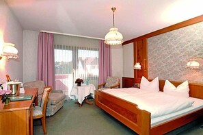 A hotel room with a bed, a desk, a chair, a small table, and a window with curtains.