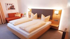 A hotel room with a bed, a nightstand, a lamp, a sofa, and a painting on the wall. - Zum Hirschen (Donaueschingen)