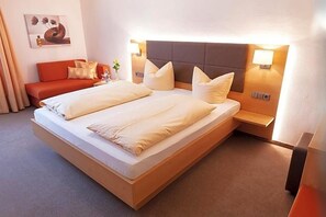 A hotel room with a bed, a nightstand, a lamp, a sofa, and a painting on the wall.