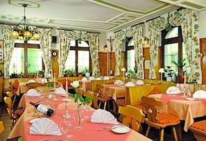 A dining area with tables set for service, a chandelier, and large windows with curtains.