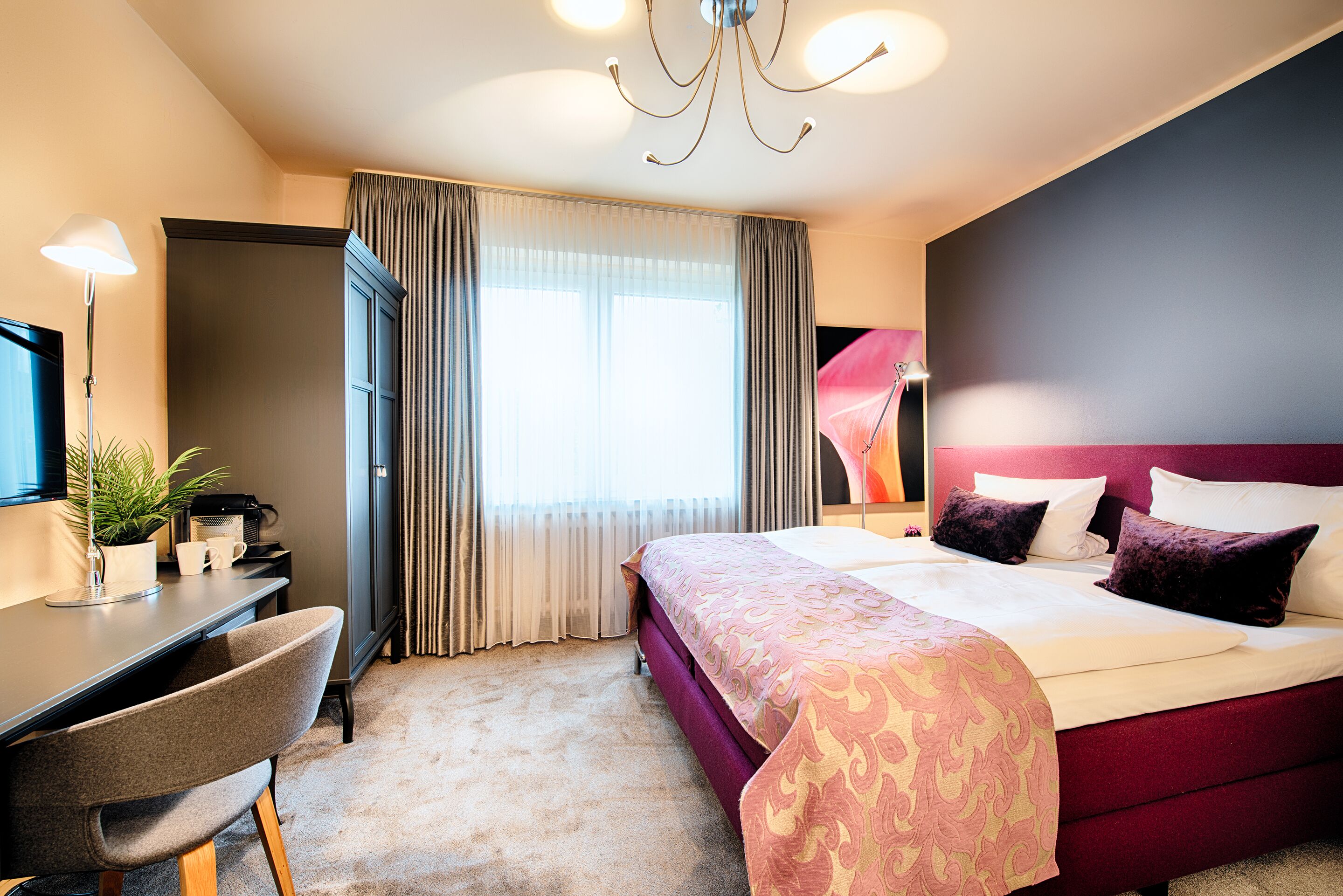 A hotel room with a bed, desk, chair, and a large window with curtains.