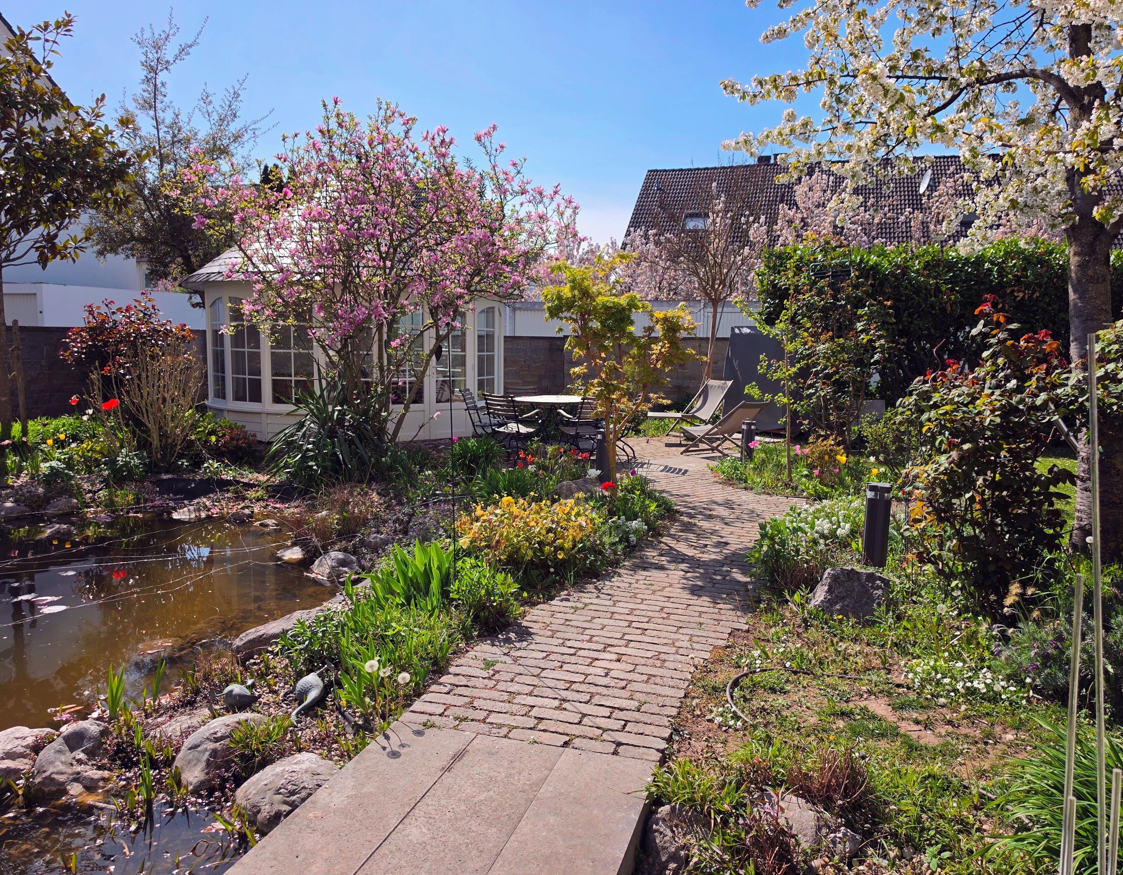 A garden with a pond, a brick pathway, and outdoor seating.