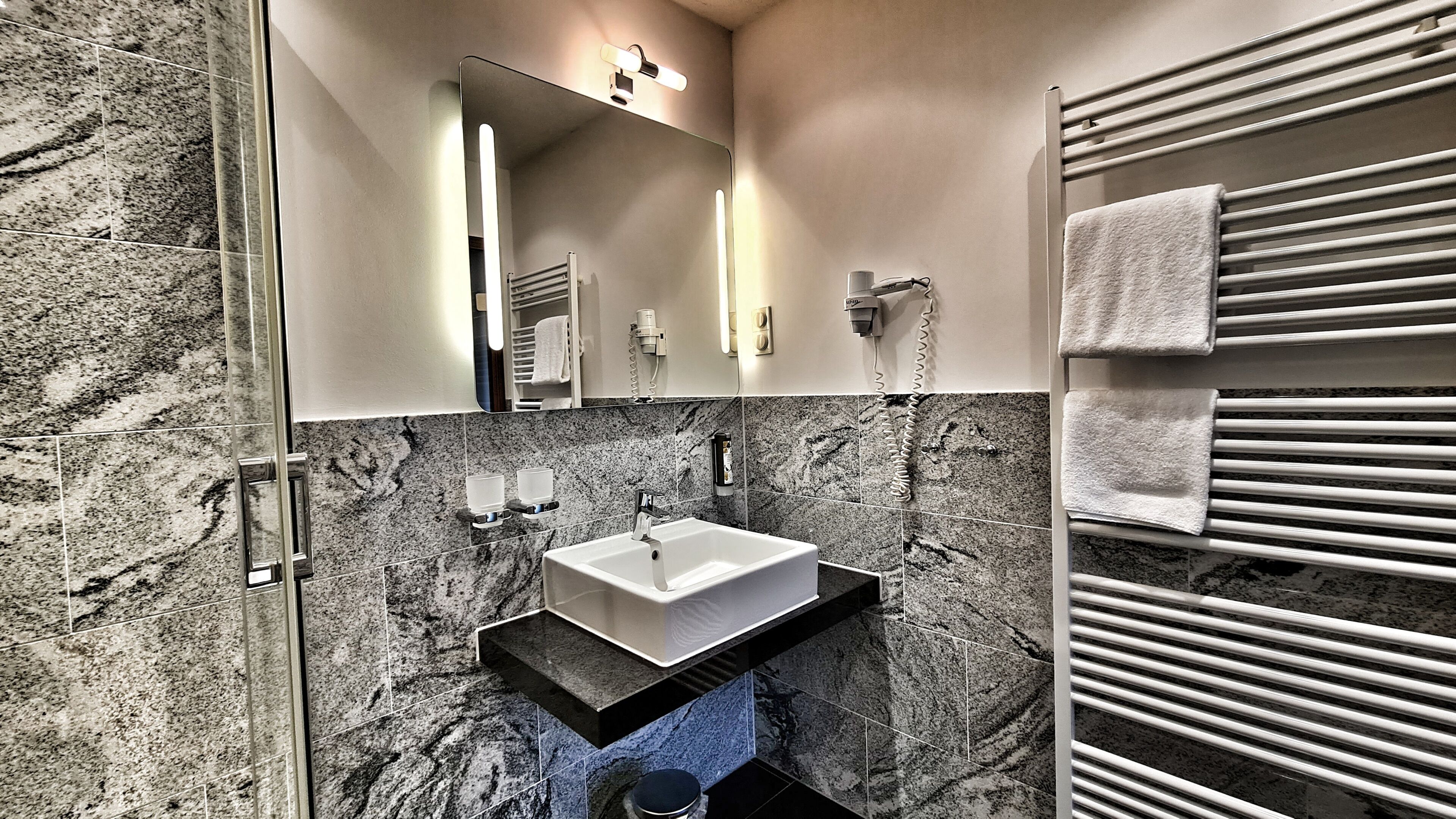Une salle de bain avec un mur en marbre, un lavabo, un miroir, un porte-serviettes et un sèche-serviettes électrique.