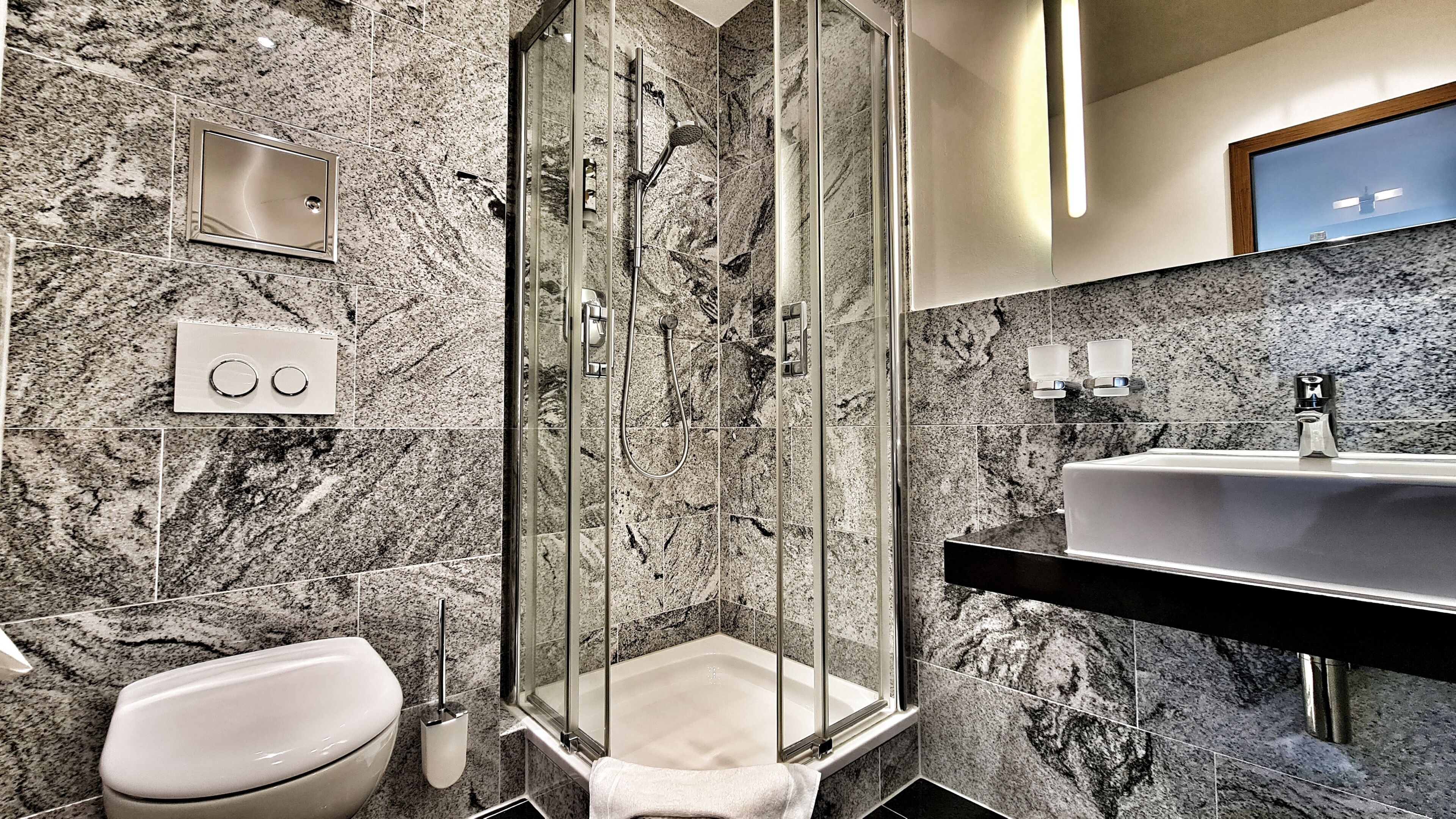 A modern bathroom with a glass-enclosed shower, a white toilet, and a marble-tiled wall.