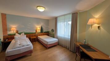 Habitación de hotel con dos camas, un escritorio, una silla, una lámpara, un cuadro en la pared y una ventana con cortinas.