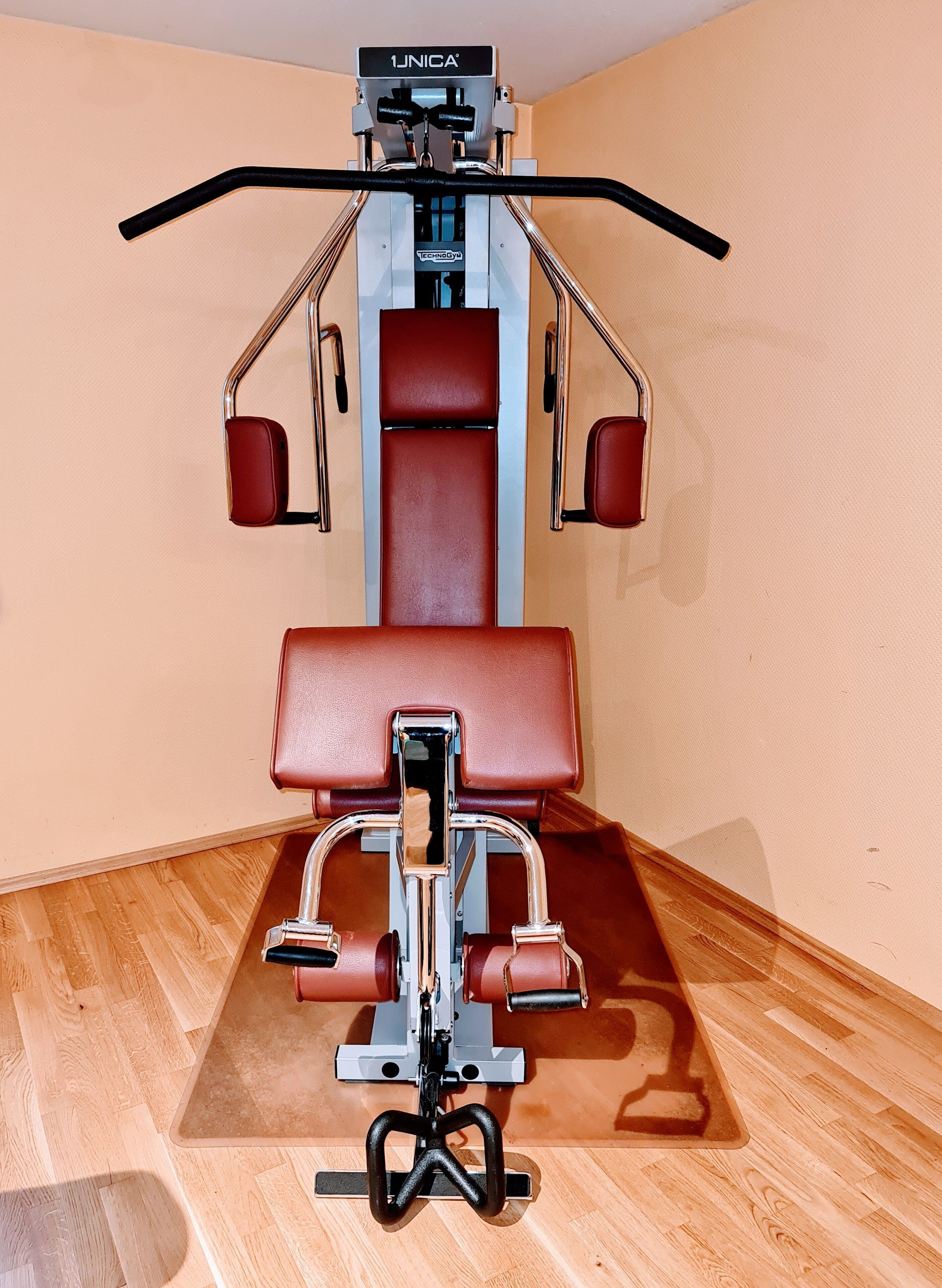 A gym with a red and black exercise machine, a wooden floor, and beige walls.