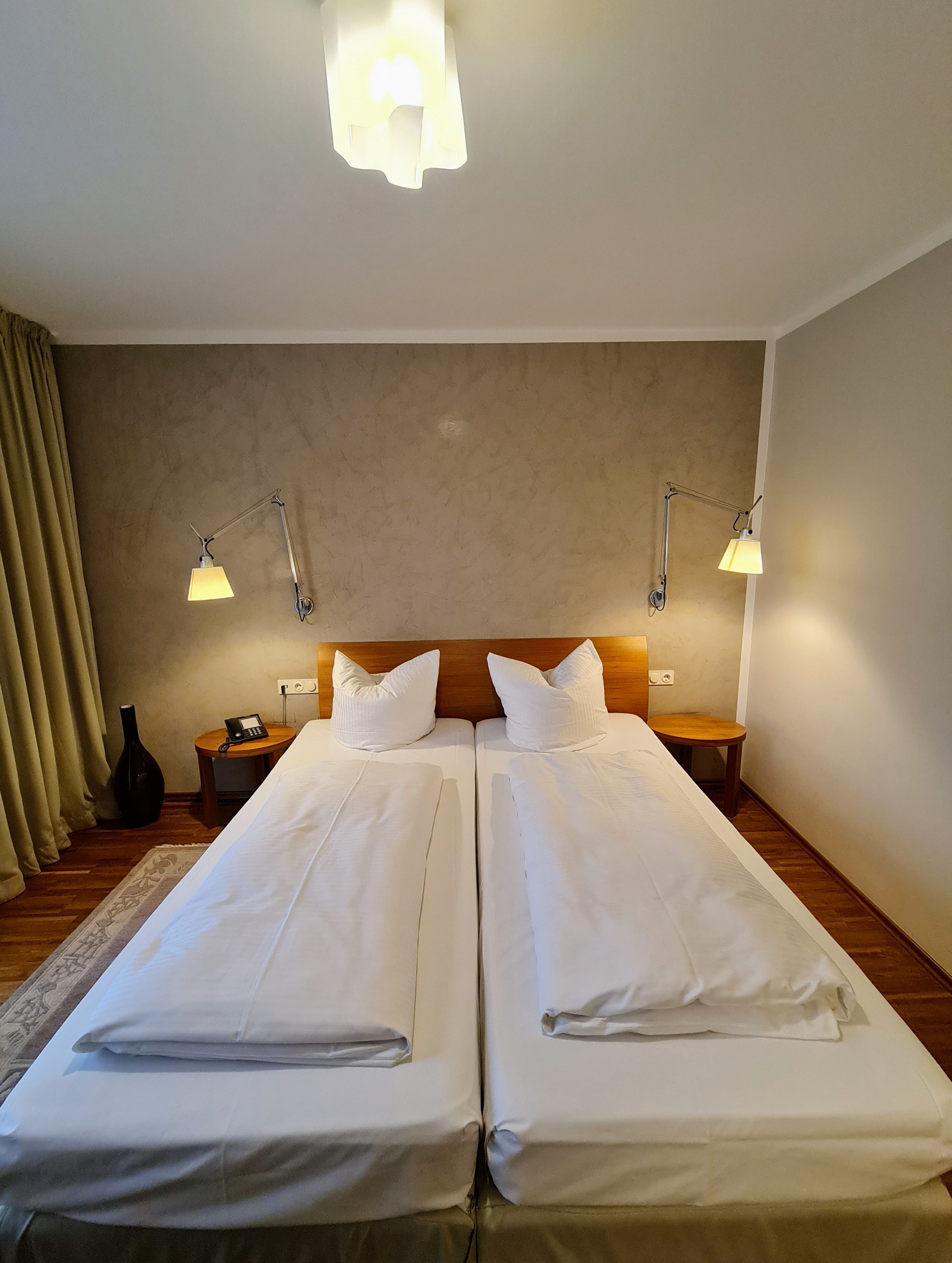 A double room with two beds, bedside tables, lamps, a telephone, and a vase on the left side.