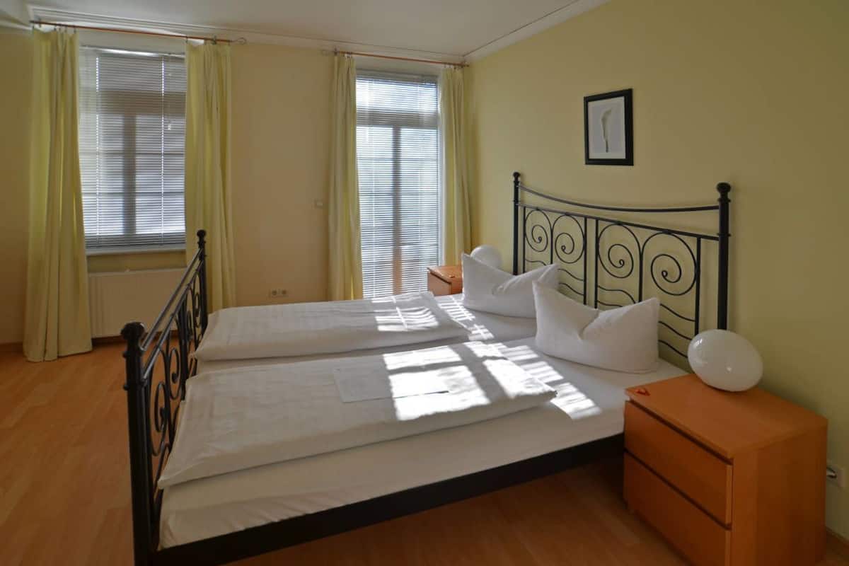 A bedroom with a double bed, two bedside tables, a window with curtains, and a framed picture on the wall.