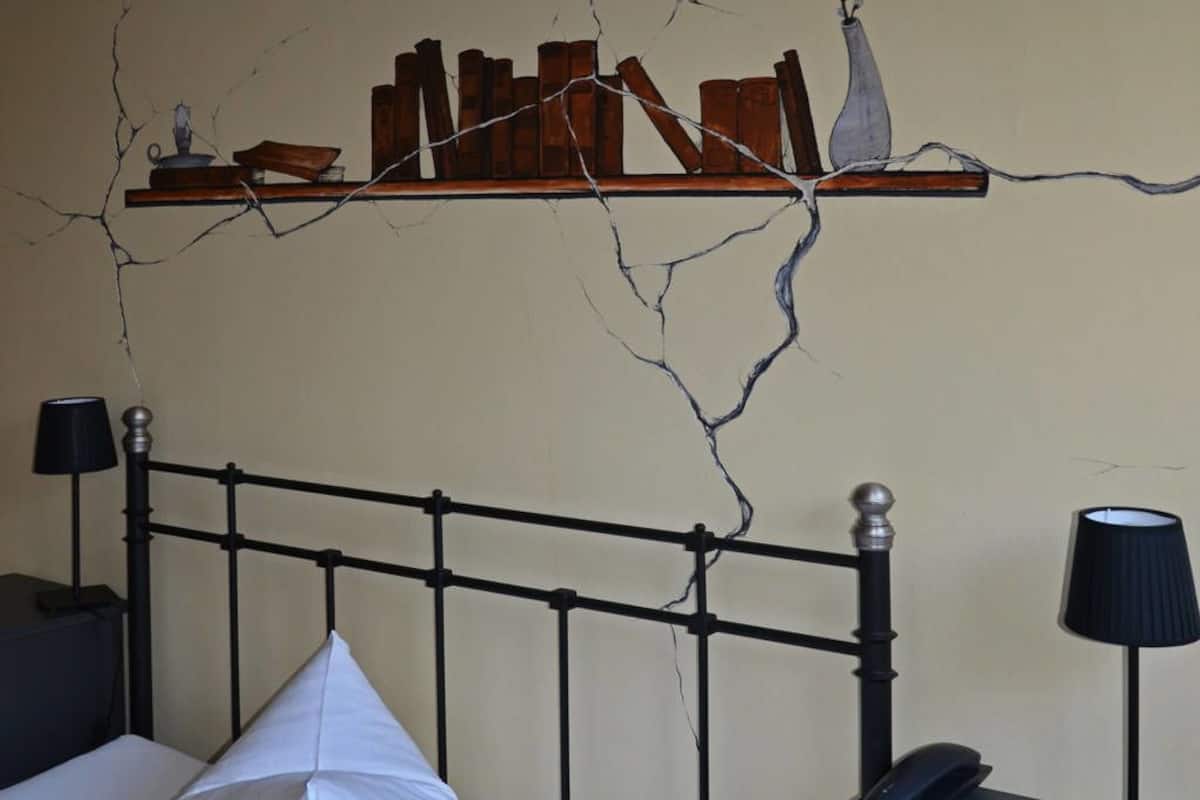 A bedroom with a bed, bedside tables, a nightstand, and a wall with a cracked pattern.