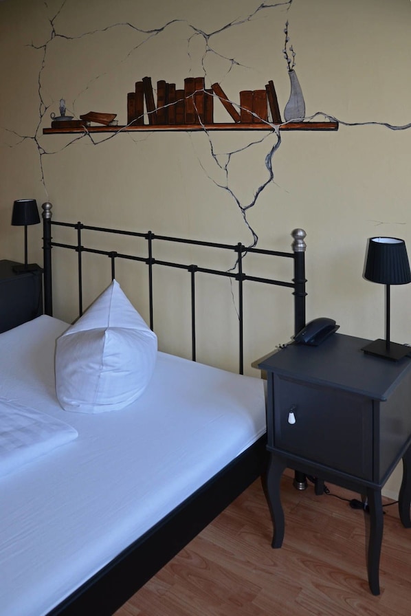 A bedroom with a bed, bedside tables, a nightstand, and a wall with a cracked pattern.