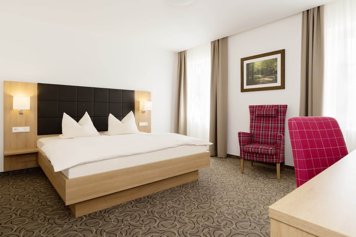 A hotel room with a bed, two bedside tables, a chair, a desk, and a framed picture on the wall.