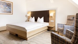 A modern bedroom with a large bed, two bedside tables with lamps, a plaid armchair, and a painting on the wall. - Gasthof Lerner (Freising)